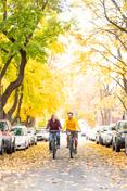 Two students ride down Greek Row in the fall, amid changing 叶子.